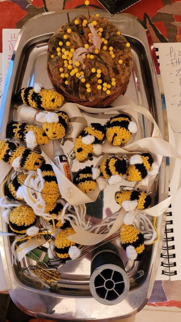 Crocheted bees on a tray in various stages of being completed, along with some pins and needles and thread..